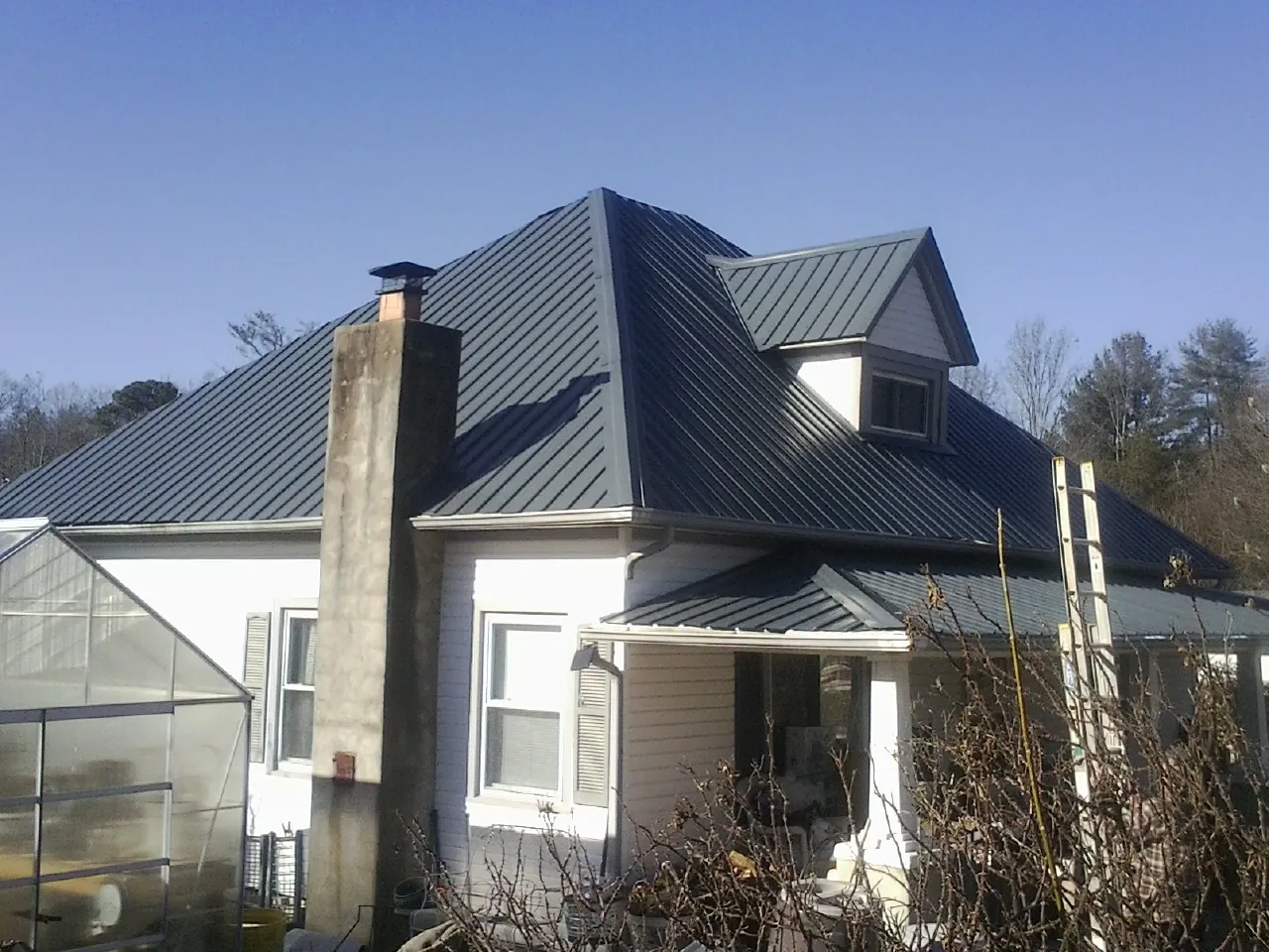 Dark blue standing seam metal roof on a white farmhouse with dormer — Slate & Tile Roof Repair by Roofing Brothers in Limington
