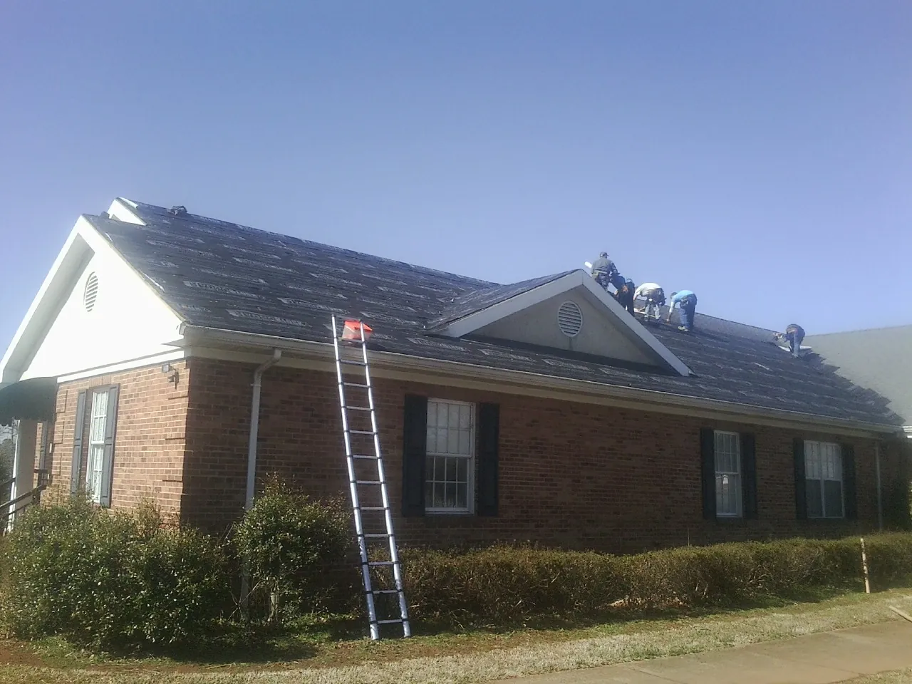 Crew tearing shingles off a brick ranch roof with a ladder set — Emergency Roof Repair work by our crew in Limington