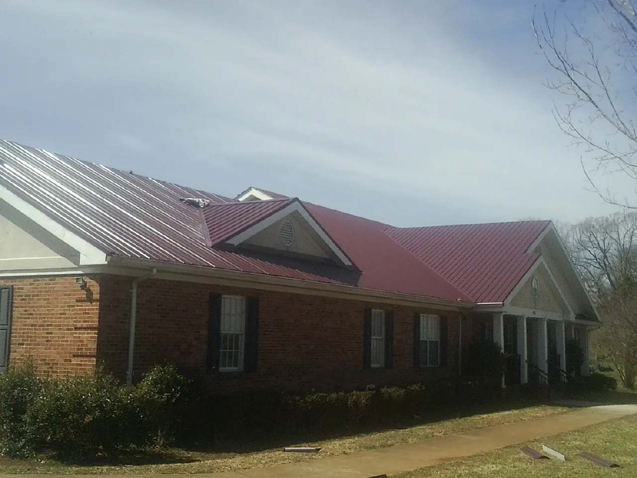 Red metal roof with gabled entries on a long brick building, from a Hail Damage Roof Repair job in Limington