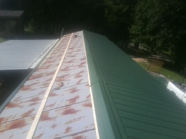 Old rusted panels beside newly installed green metal roofing — Wind Damage Roof Repair by Roofing Brothers in Limington