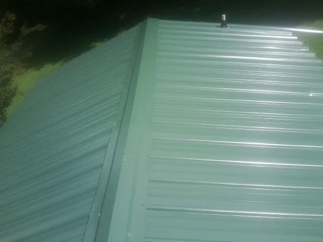 New green metal panels meeting at the ridge of a roof — Flat Roof Repair work by our crew in Limington