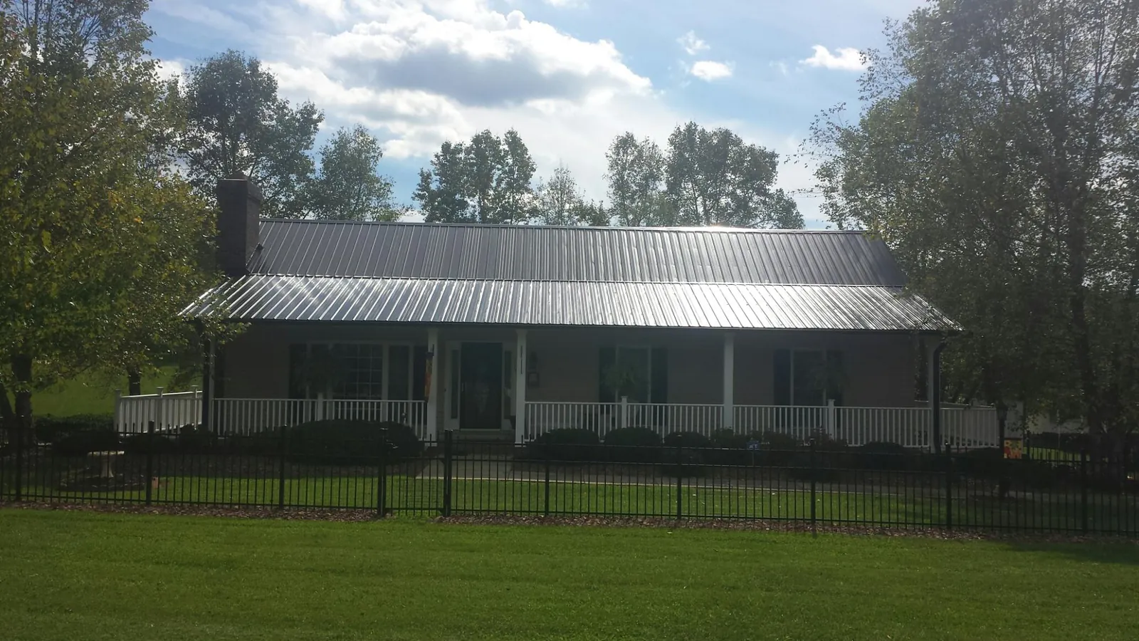 Gray metal roof on a brick ranch with a full width front porch — Gutter Guard Installation work by our crew in Limington