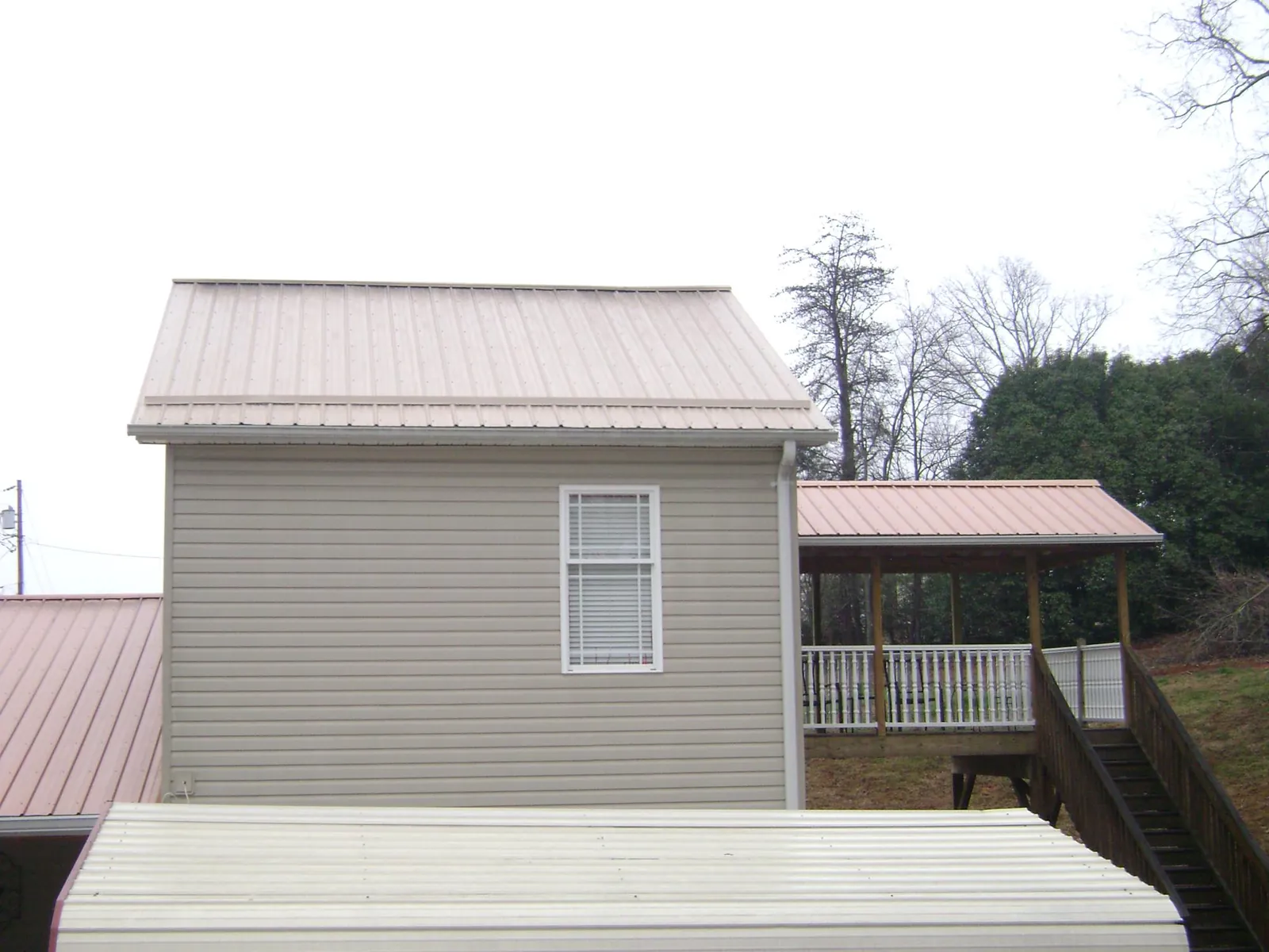 Tan metal roofs on a two story addition and attached porch, from a Roof Replacement job in Limington